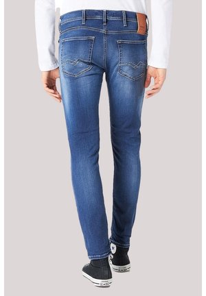 Slim-fit blauwe spijkerbroek met vervaagde details, achterzakken met stiksel, gedragen door een persoon met zwarte Converse hoge sneakers.