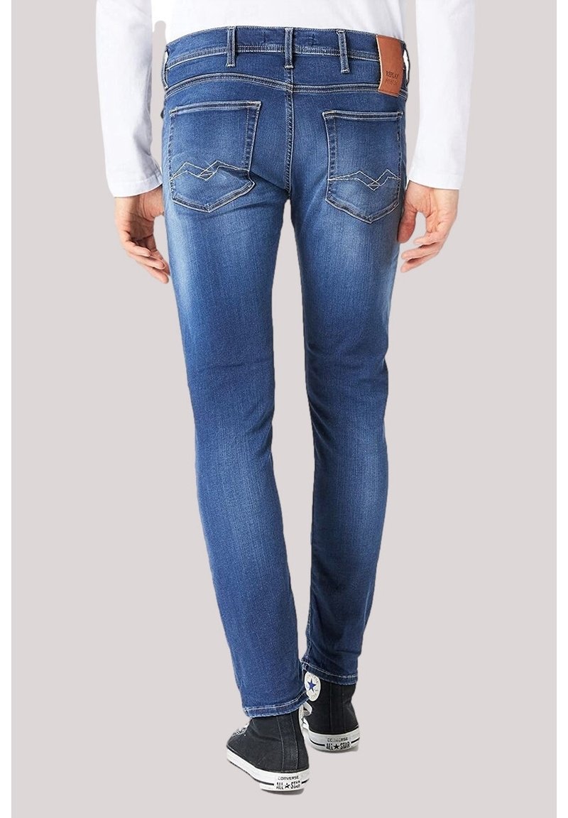 Jean slim bleu avec détails délavés, poches arrière avec coutures, porté par une personne avec des baskets montantes Converse noires.