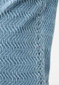 Μπλε ύφασμα με υφασμένο σχέδιο σε ζιγκ-ζαγκ και ορατή ραφή στη δεξιά πλευρά.