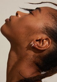 Pendientes de aro de plata con un diseño de triple banda, llevados en la oreja izquierda de una persona con piel oscura y cabello muy corto.