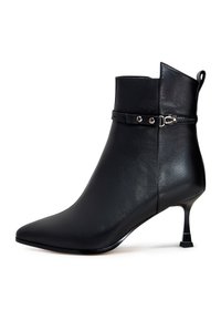 Botte de cheville en cuir noir avec un bout pointu, un talon kitten slim, et une sangle décorative avec une quincaillerie en argent autour de la cheville.