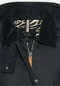 Veste noire avec col en velours côtelé, partiellement dézippée pour montrer la doublure à imprimé zèbre et l'étiquette de taille 36 avec le label tissu biologique.