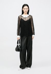 Sort blonde blonderet top med lange ærmer lagdelt over en sort kjole, kombineret med vide sorte læderbukser, hvid krave som accent og en sort minitaske.