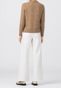 Suéter de lana marrón con cuello redondo, dobladillo acanalado y mangas largas. Combinado con unos jeans blancos de tiro alto y anchos, y zapatos beige.