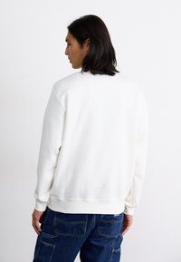 Hvid fleece sweatshirt med en rund halsudskæring og ribbede manchetter, kombineret med mørkeblå denim jeans. Stoffet ser blødt ud med en glat tekstur.