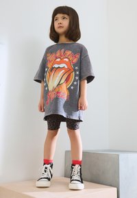 Szürke, túlméretezett Rolling Stones grafikás póló, leopárdmintás kerékpáros nadrág, piros bokazokni és fekete magas szárú tornacipő fehér talppal.