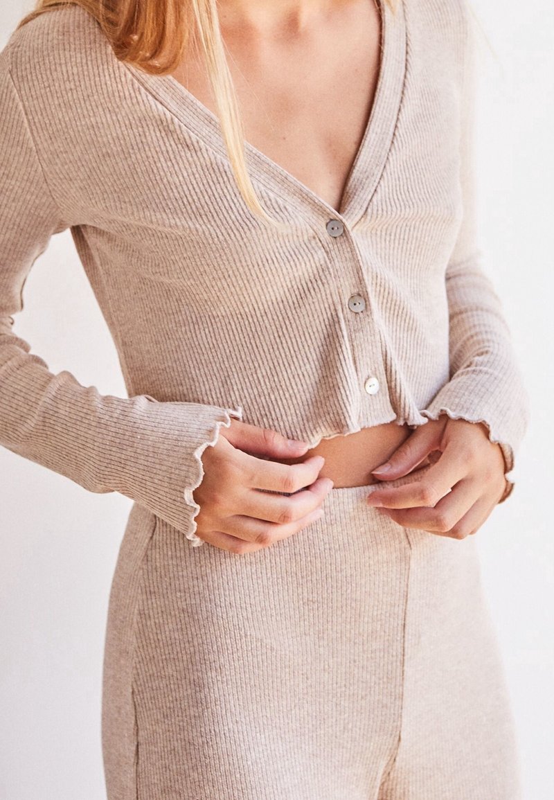 Béžový pruhovaný krátký top s výstřihem do V, třemi knoflíky a volánkovými rukávy, spárovaný s odpovídajícími pruhovanými kalhotami s vysokým pasem.