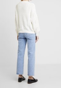 Gruba biała dzianinowa sweter z okrągłym dekoltem, w połączeniu z jasnoniebieskimi prostymi dżinsami. Sweter ma strukturalne wzory i ściągacze przy mankietach.