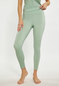 Világoszöld leggings, rugalmas, sima anyagból. Magas derekú design, amelyeknek nincsenek kiemelkedő mintái. Tiszta, formás silhuett.
