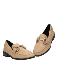 Mocasines de ante beige con un tacón negro bajo. Presentan un hardware decorativo de bucle dorado en la parte frontal y un detalle de costura en contraste.