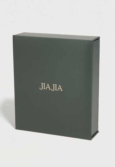 Σκούρο πράσινο ορθογώνιο κουτί σε όρθια θέση με την ένδειξη "JIA JIA" εκτυπωμένη σε χρυσό, στο κέντρο της μπροστινής πλευράς, σε απλό φόντο.