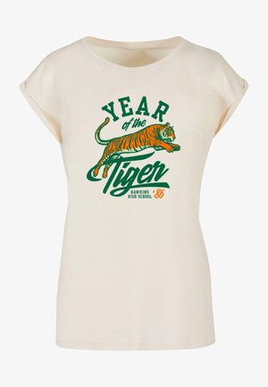 Tricou de culoare crem, cu mâneci scurte răsucite. Prezintă un text grafic verde și portocaliu: "ANUL Tigrului" și o ilustrație vibrantă a unui tigru.
