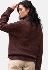 Brązowy sweter dziewiarski z wysokim kołnierzem, ściągaczami na rękawach i luźnym krojem, charakteryzujący się teksturowanym wykończeniem i delikatnym połyskiem.