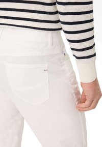 Witte denim jeans met een achterzak met een klein "Brax" logo, gestyled met een gestreepte trui. Focus op het schone ontwerp en de textuur.