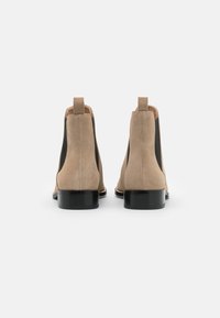 Botines de ante beige con paneles laterales de elástico negro, punta redondeada y tacón bajo cuadrado, que incluyen una lengüeta en la parte posterior.