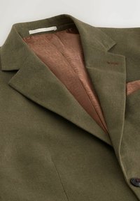Blazer vert texturé avec doublure en satin marron à motif, revers cranté et fermeture à un bouton sombre.