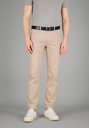 Beige Chinos aus einem Baumwollmix mit fünf Taschen, vorderem Knopfverschluss und geradem Bein. Getragen mit einem grauen T-Shirt und weißen Sneakers.