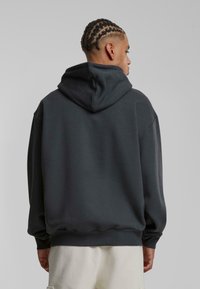 Mørkegrå pullover hoodie med en stor hætte, ribbede manchetter og kant. Stoffet ser blødt og struktureret ud, med en afslappet pasform og minimal detaljering.