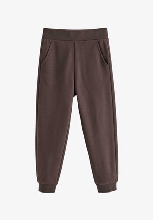 Unge barn iført brun hue, denimjakke over blå langærmet skjorte, brune bukser og røde og hvide sneakers, stående mod hvid baggrund.