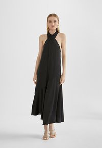 Black halter dress featuring a flowing silhouette, layered design, soft fabric, and a floor-length hem. Complemented by strappy gold sandals.