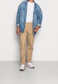 Dżinsowa kurtka o luźnym kroju, zestawiona z khaki spodniami cargo i białymi trampkami. Kluczowe cechy to kieszenie w spodniach oraz klasyczny styl.