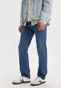 Blå denimjeans med rak skärning, i en klassisk design. Barns ihop med en ljusblå denimjacka och vita sneakers med svarta accenter.