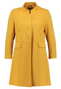 Vaaleankeltainen, teksturoitu takki, jossa on korkea kaulus, etutaskut ja suora leikkaus. Varustettu piilotetulla nappilinjalla. Pitkät hihat.