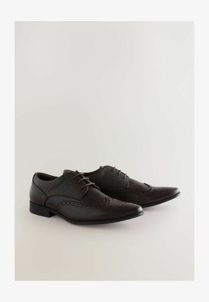 Zapatos de vestir de cuero marrón con punta afilada, detalles de brogue y cordones de cuero. El diseño presenta un upper texturizado y una suela plana de goma.