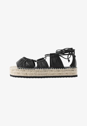 Sandalo espadrilla in pelle nera con suola intermedia in juta intrecciata, caratterizzato da cinturini arrotondati e design con lacci. Suola piatta in gomma.