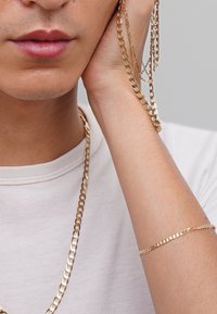 Gold chains layered around a neck and wrist, featuring a flat, shiny texture with links in a classic design, against a neutral background.