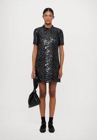 Musthave lühikeste varrukatega must kleit tekstuursete sädelevate detailidega, krae, reie kõrgus, koos musta koti ja dekoratiivsete aktsentidega kingadega.