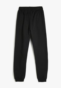 Pantalones de chándal negros hechos de una tela suave, con una cinturilla ancha y elástica y puños ajustados en los tobillos. Sin patrones ni adornos.