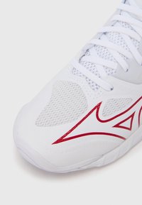 Λευκό αθλητικό παπούτσι με λεπτομέρειες από δίχτυ, υλικό από υφασματισμένο συνθετικό με υφή και έντονο κόκκινο λογότυπο. Διαθέτει κορδόνια και σκληρή σόλα.