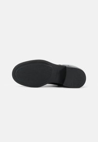 Suola di scarpa in gomma nera con superficie texture e tallone rinforzato. Forma leggermente curvata, bordi lisci, con un'iscrizione del marchio.