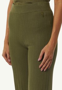 Geribbelde olijfgroene leggings met een hoge tailleband en een subtiel logo-detail. Zachte textuur en nauwsluitend ontwerp benadrukken de lichaamsvorm.
