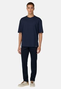 Jūras spēku krāsas kokvilnas T-krekls ar īsām piedurknēm un brīvu piegriezumu, apvienots ar atbilstošām šaurām jūras spēku krāsas biksēm un bežām kedām ar brūniem akcentiem.