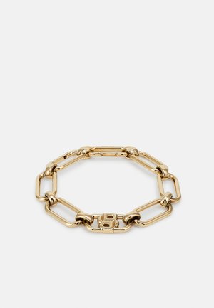 Bracelet en métal doré avec de grandes maillons de chaîne entrelacés. Présente un accent central avec un logo gravé, une texture lisse et une finition polie.