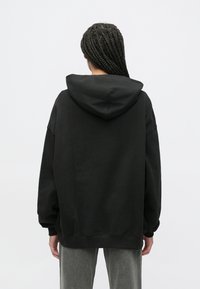Čierna oversize mikina s kapucňou na šnúrku, rebrovanými manžetami a lemom; bavlnená zmes látky, hladká textúra a minimalistický dizajn.