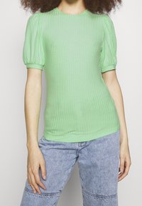 Top verde a coste con maniche corte e tondo colletto, abbinato a jeans a vita alta di colore azzurro chiaro.