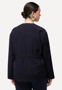 Granatowa, długosleeve kurtka o luźnym kroju, elastycznym pasie i gładkiej fakturze. Prosty design z okrągłym dekoltem i bez ozdób.