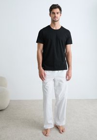 T-shirt noir à manches courtes associé à un pantalon de pyjama à rayures blanches. Le tissu semble doux et confortable ; la coupe est décontractée.