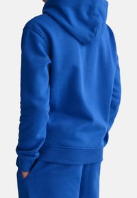 Blå huvtröja med en mjuk textur, ribbade ärm- och fållkanter. Har en rymlig huva och en klassisk design, i kombination med matchande byxor.