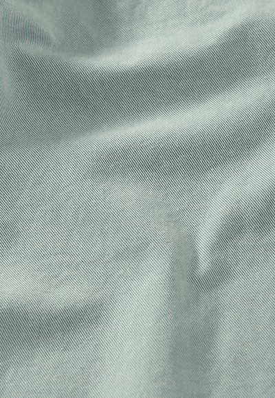 Κοντινό πλάνο υφάσματος ανοιχτού γκρι με λεπτή διαγώνια ραβδωτή υφή και διακριτικές πτυχές που δημιουργούν απαλές σκιές.