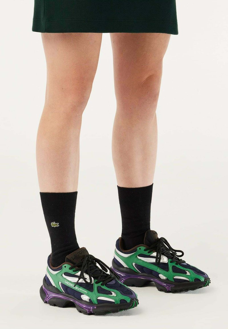 Chaussettes de sport noires associées à des baskets vertes et bleu marine avec un mesh texturé et des superpositions en synthétique, accentuées de détails violets et blancs.