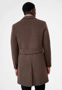 Brown wool coat featuring a tailored design, a belted waist, and buttoned cuffs, with a textured finish and a slight sheen.