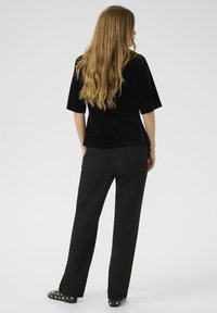 Top in velluto nero con maniche corte abbinato a pantaloni neri a gamba dritta e scarpe nere decorate. Modello visto da dietro.