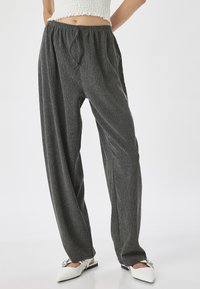 Grijze, gestructureerde, wijde broek met een elastische tailleband en strikdetail, gecombineerd met witte muiltjes met een spitse neus en een gespsluiting.