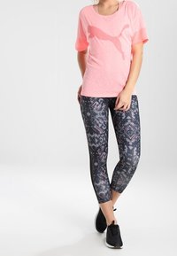 Różowa koszulka sportowa z krótkim rękawem z dużym logo Puma, zestawiona z wzorzystymi czarnymi legginsami z geometrycznymi wzorami i różowymi akcentami.