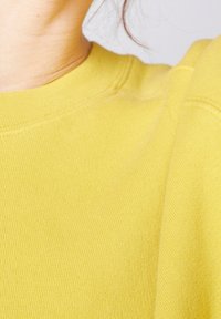 Gul bomullströja med klassisk rund hals. Tyget är mjukt med en slät textur och synliga sömmar längs halsringningen.