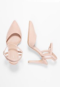 Nude-vaaleet korkokengät, joissa on kärjellinen muoto, samettinen pinta ja ohut nilkkaremmi. Varustettu läpinäkyvällä kannalla ja pehmeällä sisävuorella.